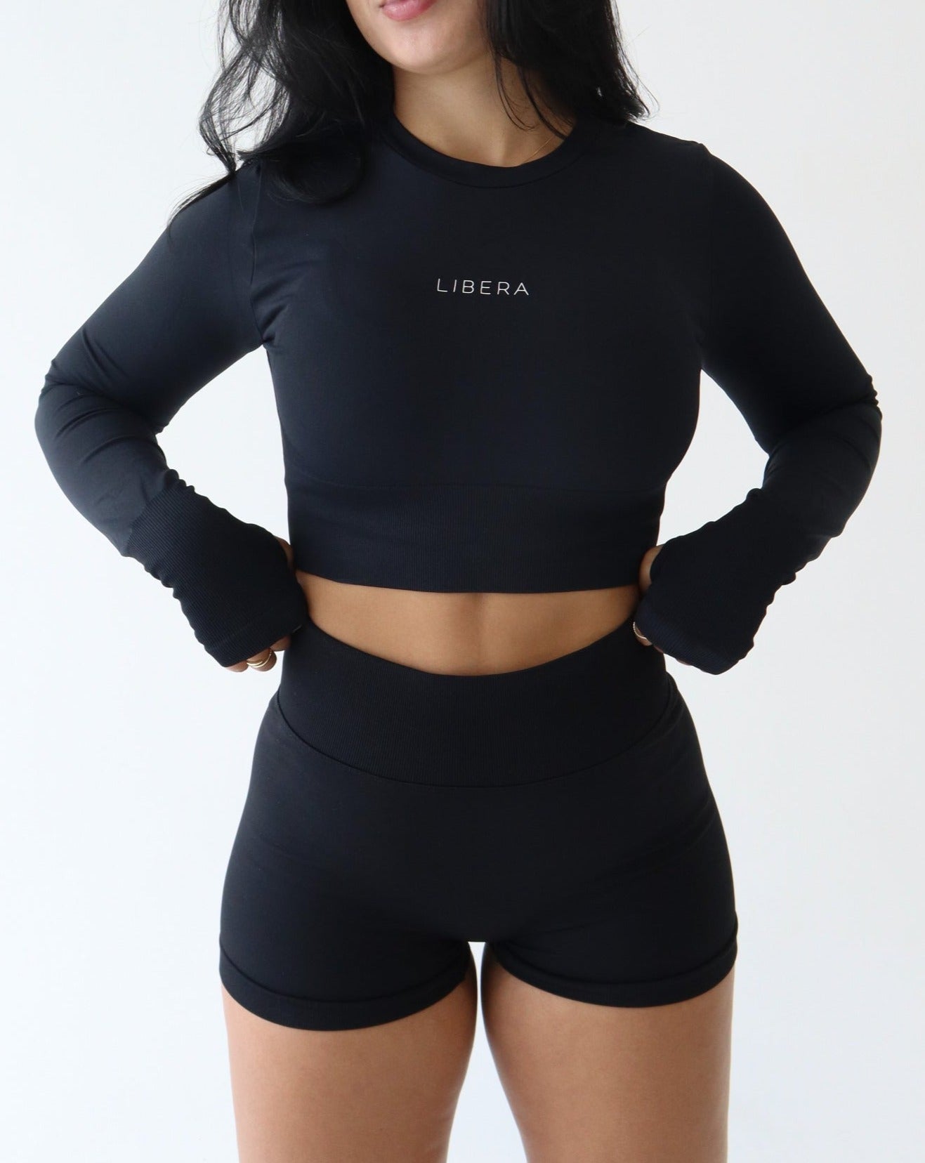 Magnify Long Sleeve Crop - BLACK - LIBERA Fitness Apparel. Stay cool and stylish during workouts with our MAGNIFY Long Sleeve Crop Top. Featuring a crew neckline and thumbholes, it offers a secure fit. Perfect for low-impact activities. Pair with our MAGNIFY seamless bottoms.